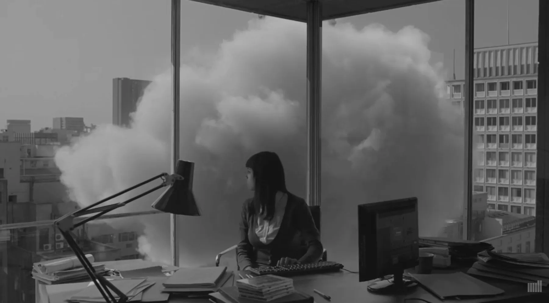 A woman at her desk looks out of an office window at a huge cloud pressed up against the glass.